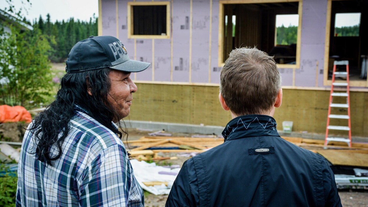 Deux hommes vus de dos devant une maison en construction.