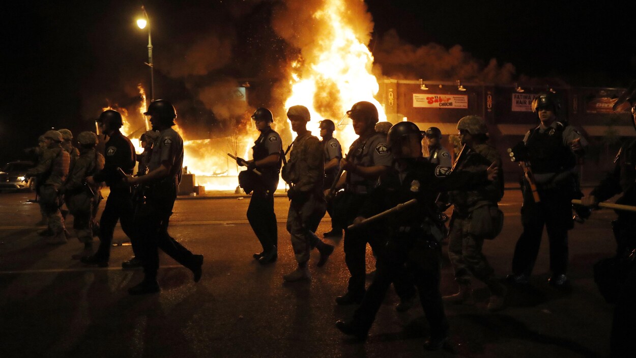 Des policiers dans la rue devant un bâtiment en flammes.