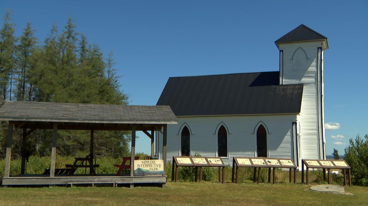 Une église extérieur et une air de repos de tables de pique-nique. «Minudie Interpretive Park» est écrit sur un écriteau.