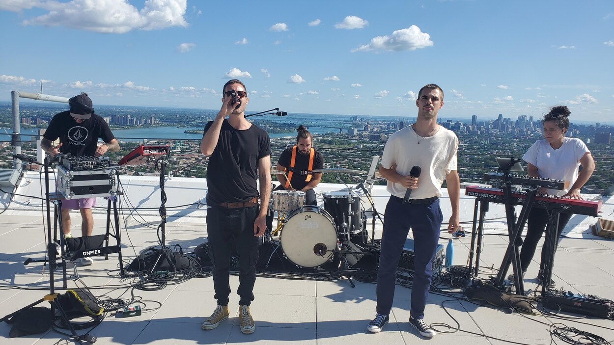 Le chanteur tient un micro et est entouré de musciens et musicienne.
