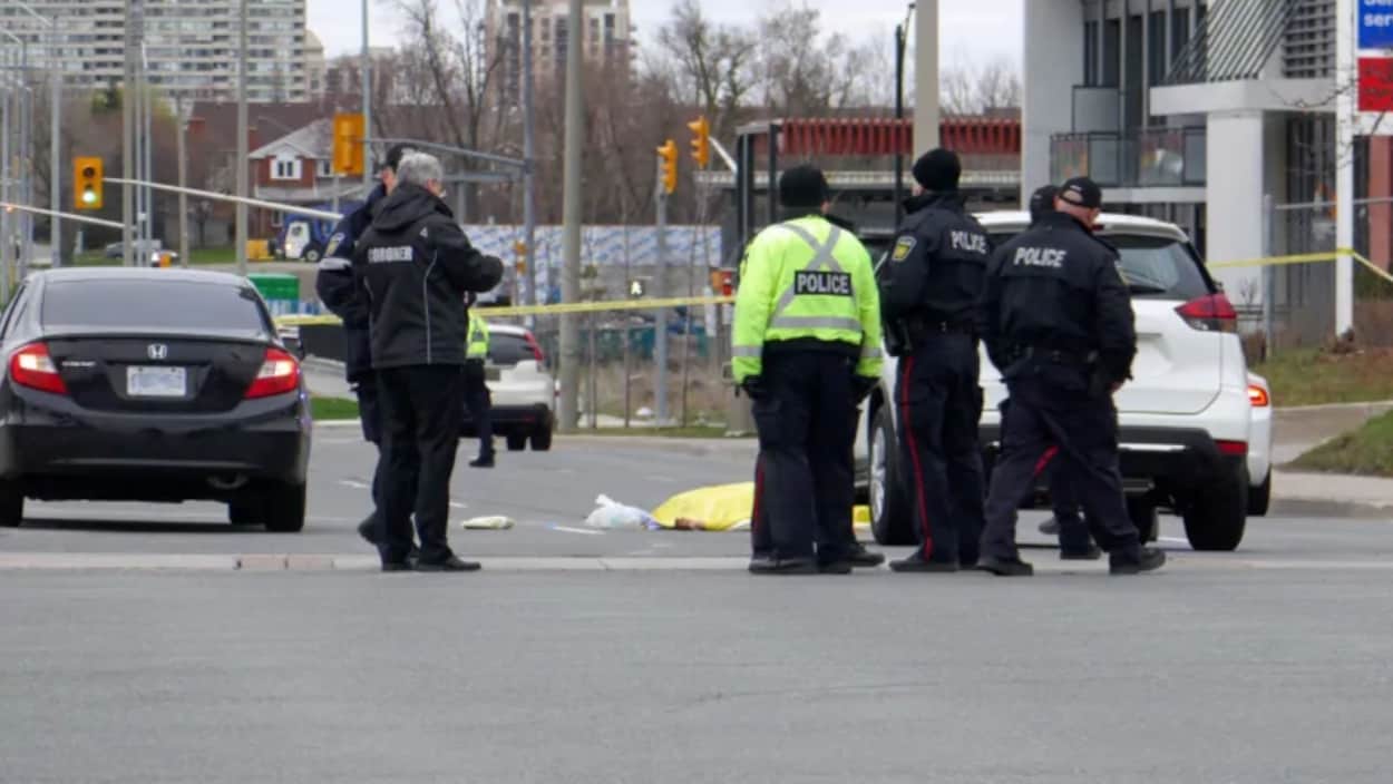 Photo de policiers se tenant debout dans une rue près de véhicules et d'une banderole de police jaune.