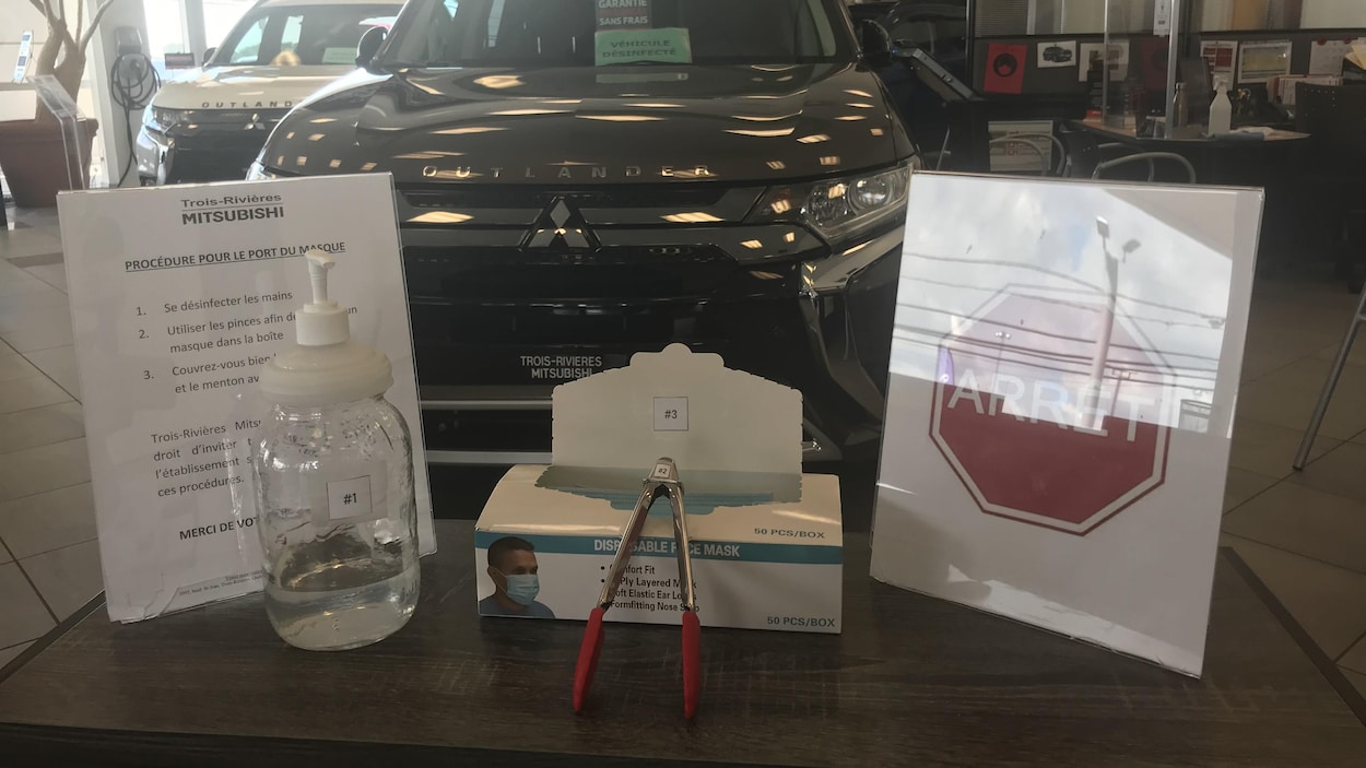 Une boîte de masques et du désinfectant à mains sur une table à l'entrée. Une voiture en arrière plan.