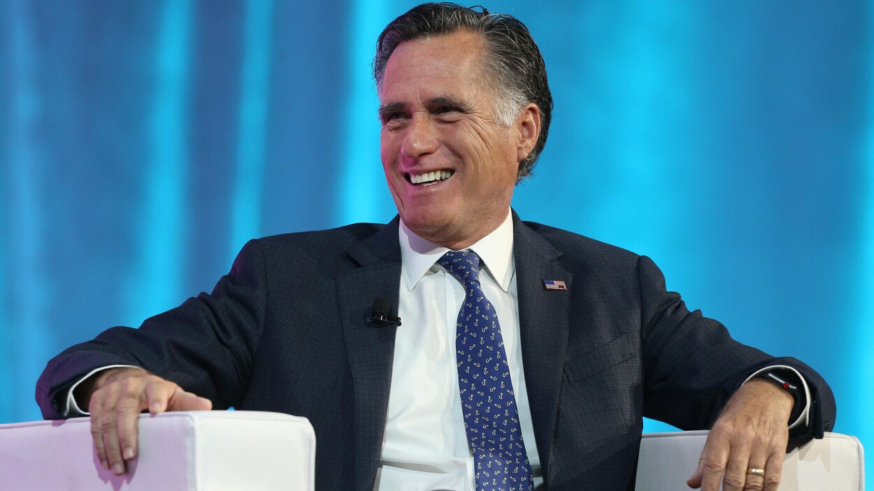 Mitt Romney est assis dans un fauteuil. Il sourit.