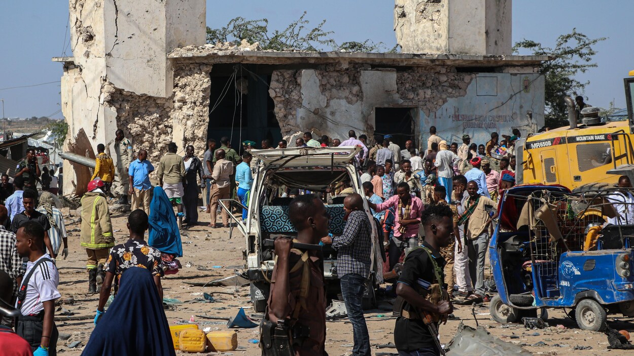 Une place chaotique où se mélangent passants et voitures devant des ruines