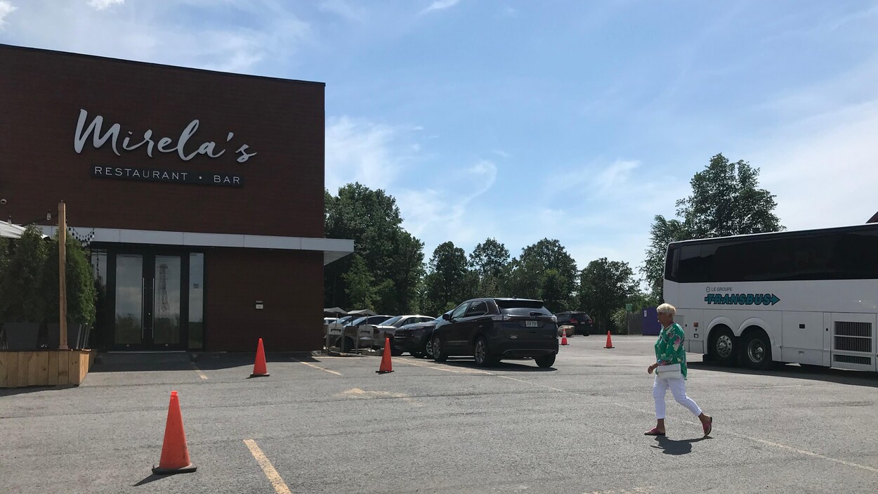 Un autobus stationné à côté d'un restaurant. Une femme marche dans le stationnement.