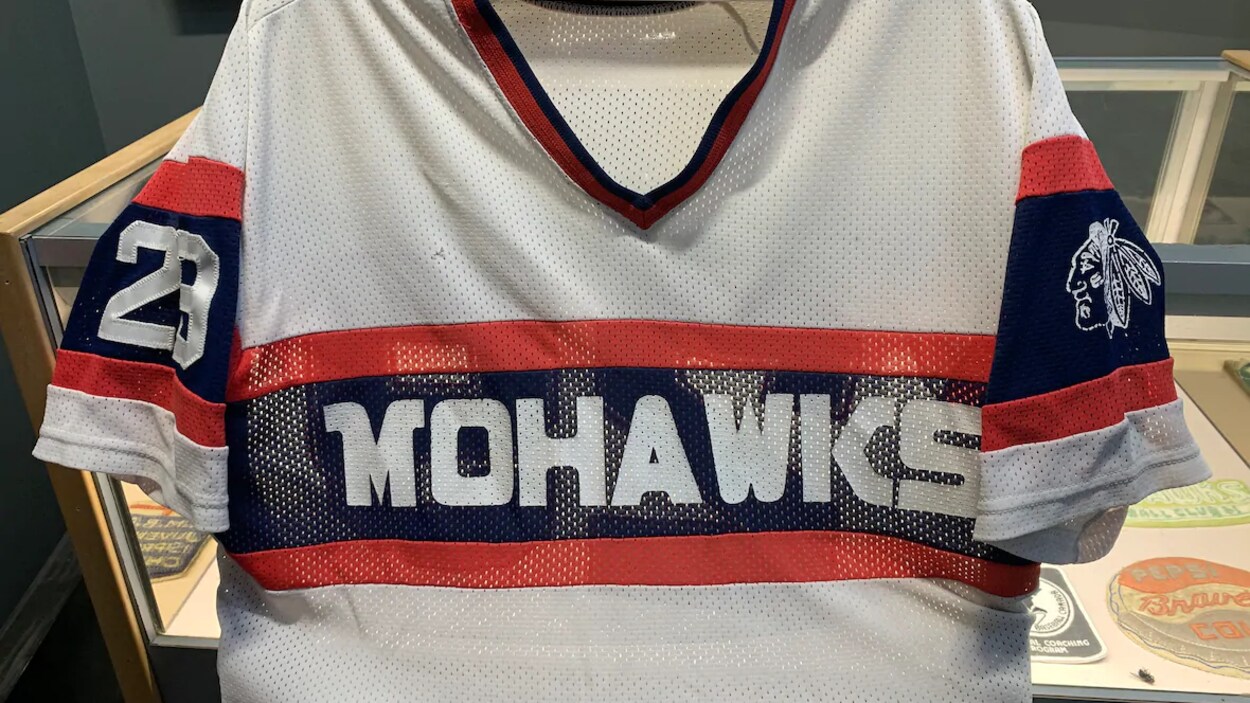 Un chandail de baseball où il est écrit en gros sur le devant Mohawks. Sur la manche gauche, on voit un dessin représentant la tête d'un autochtone avec des plumes sur sa tête.
