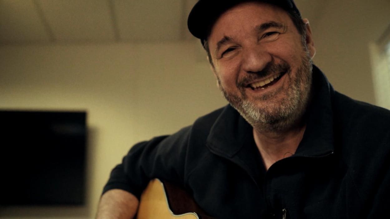 Paul Piché assis tient une guitare