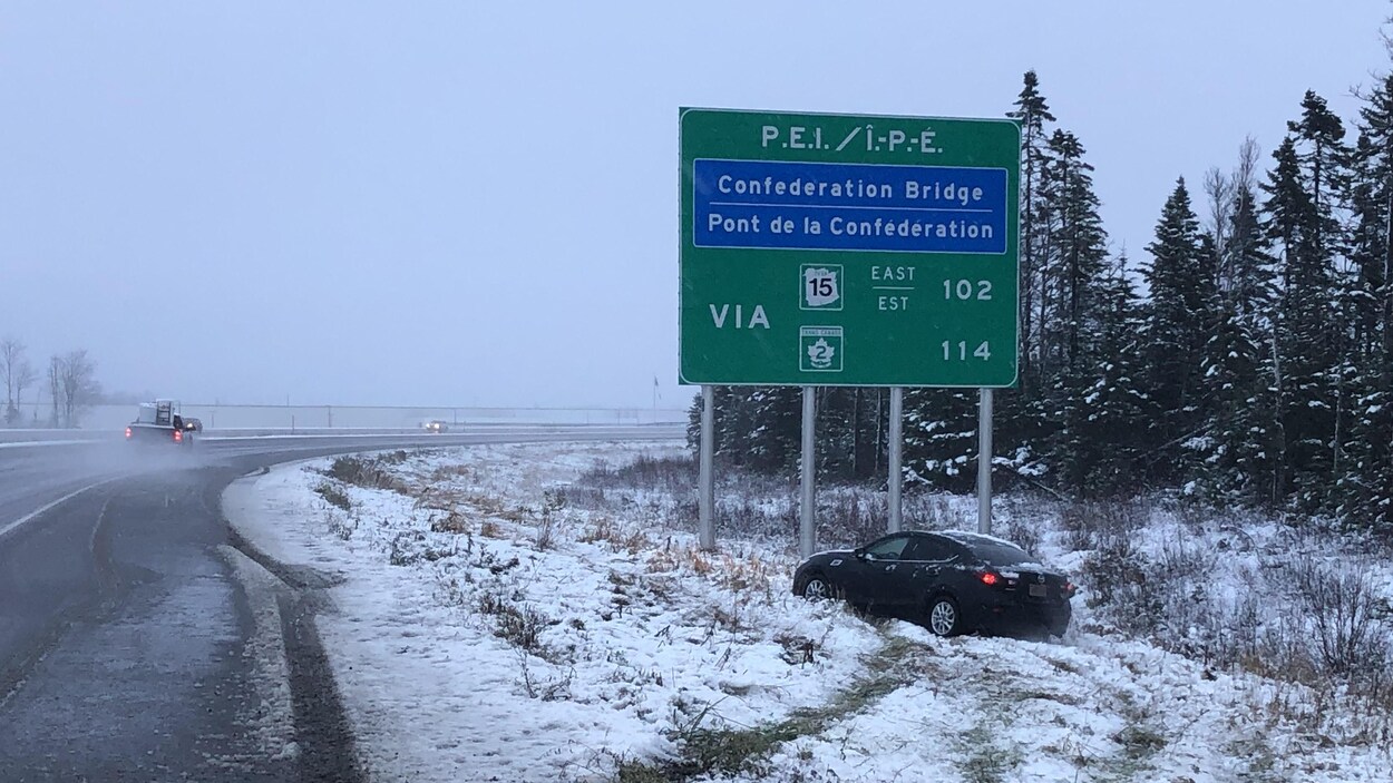 Une voiture qui a dérapé et quitté la chaussée est arrêtée en bas du talus, devant un grand panneau indicateur.