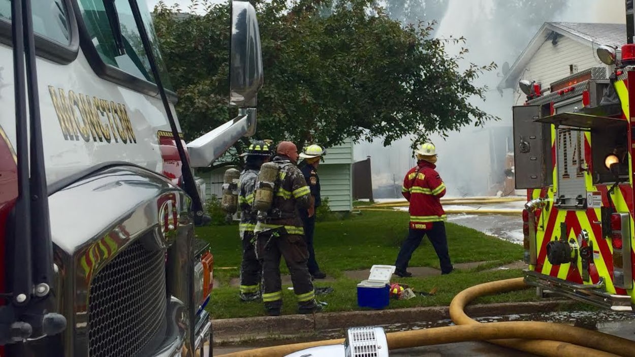 Un groupe de pompiers devant une maison qui dégage de la fumée Un groupe de pompiers devant une maison qui dégage de la fumée