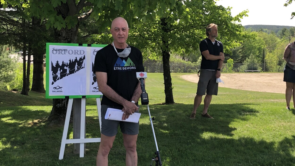 Claude Dallaire parle au micro devant une pancarte.