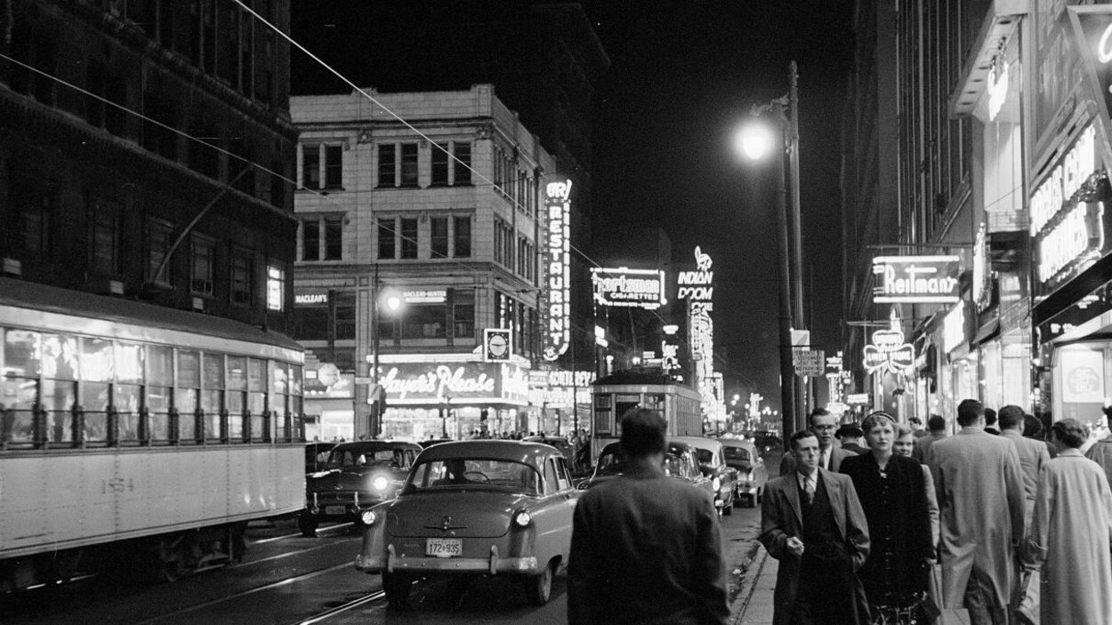 Animation au centre-ville de Montréal avec les enseignes illuminées, des gens se déplaçant sur le trottoir et des tramways qui passent au centre de la rue.