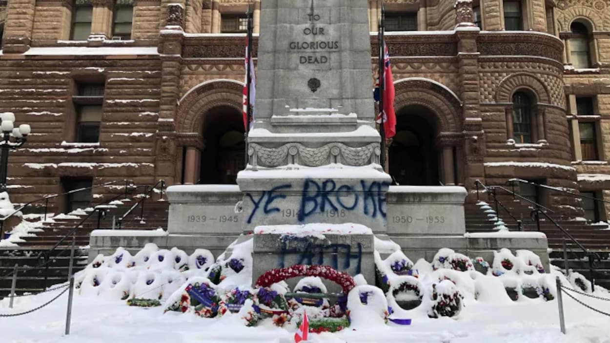 Le monument commémoratif devant l'ancien hôtel de ville de Toronto entouré de gerbes de fleurs sous la neige, sur lequel quelqu'un a écrit avec une bombe de peinture : "Ye broke faith".