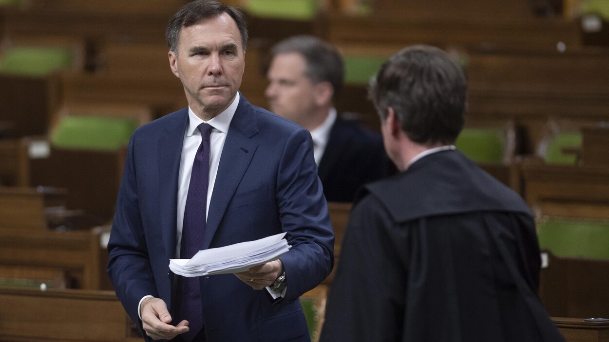 Bill Morneau remet une pile de documents à un employé des Communes.