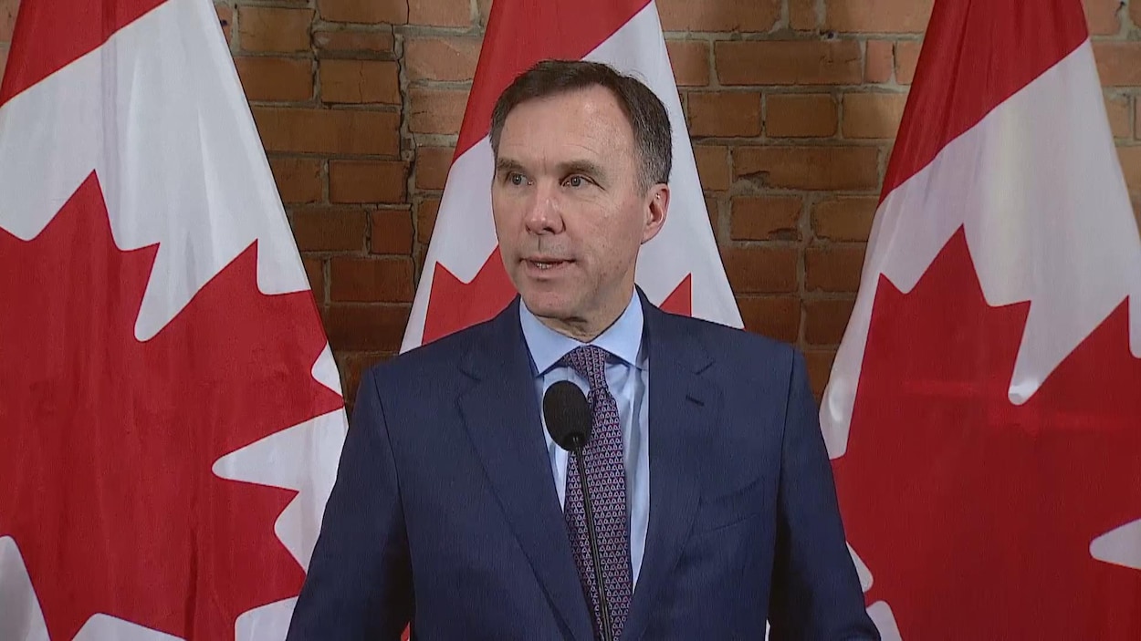 Plan moyen de Bill Morneau en conférence de presse devant trois drapeaux du Canada.