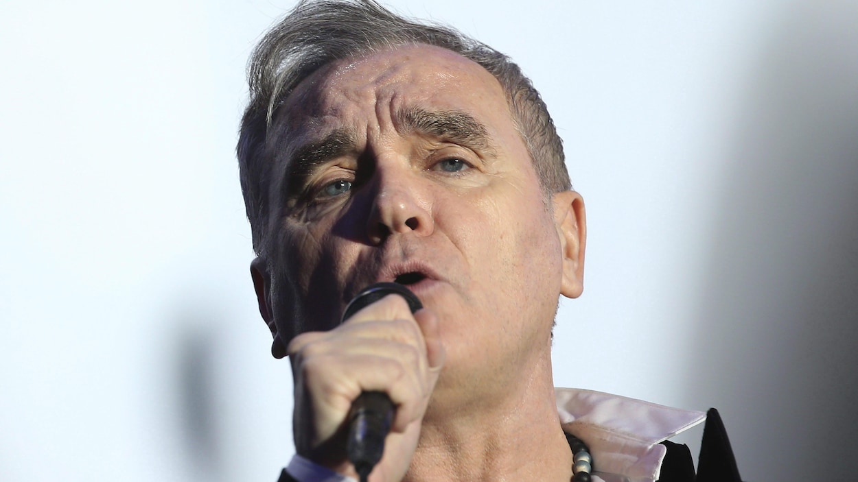 Le chanteur Morrissey en concert tient son micro à la main en faisant face à l'appareil photo.