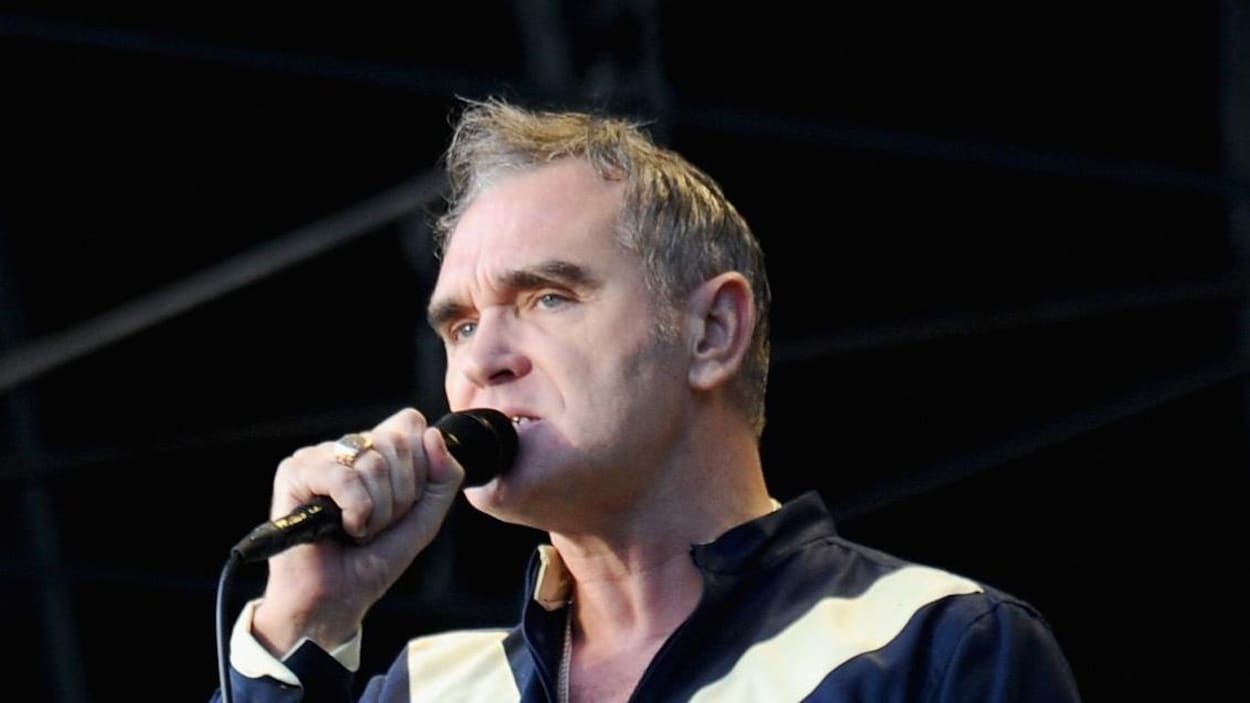 Le chanteur Morrissey tient un micro dans sa main droite et donne un spectacle devant une foule.
