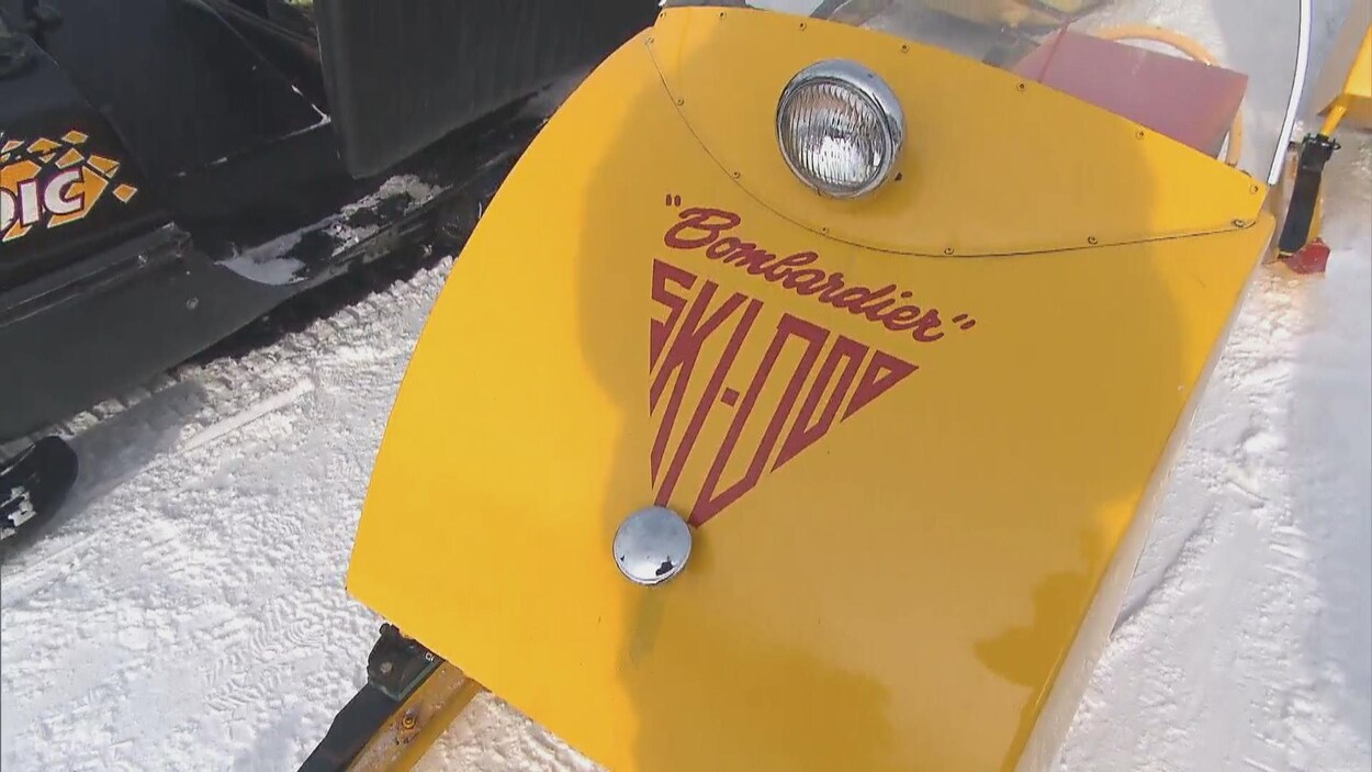 Une petite motoneige antique de couleur jaune est garée à proximité d'un sentier.