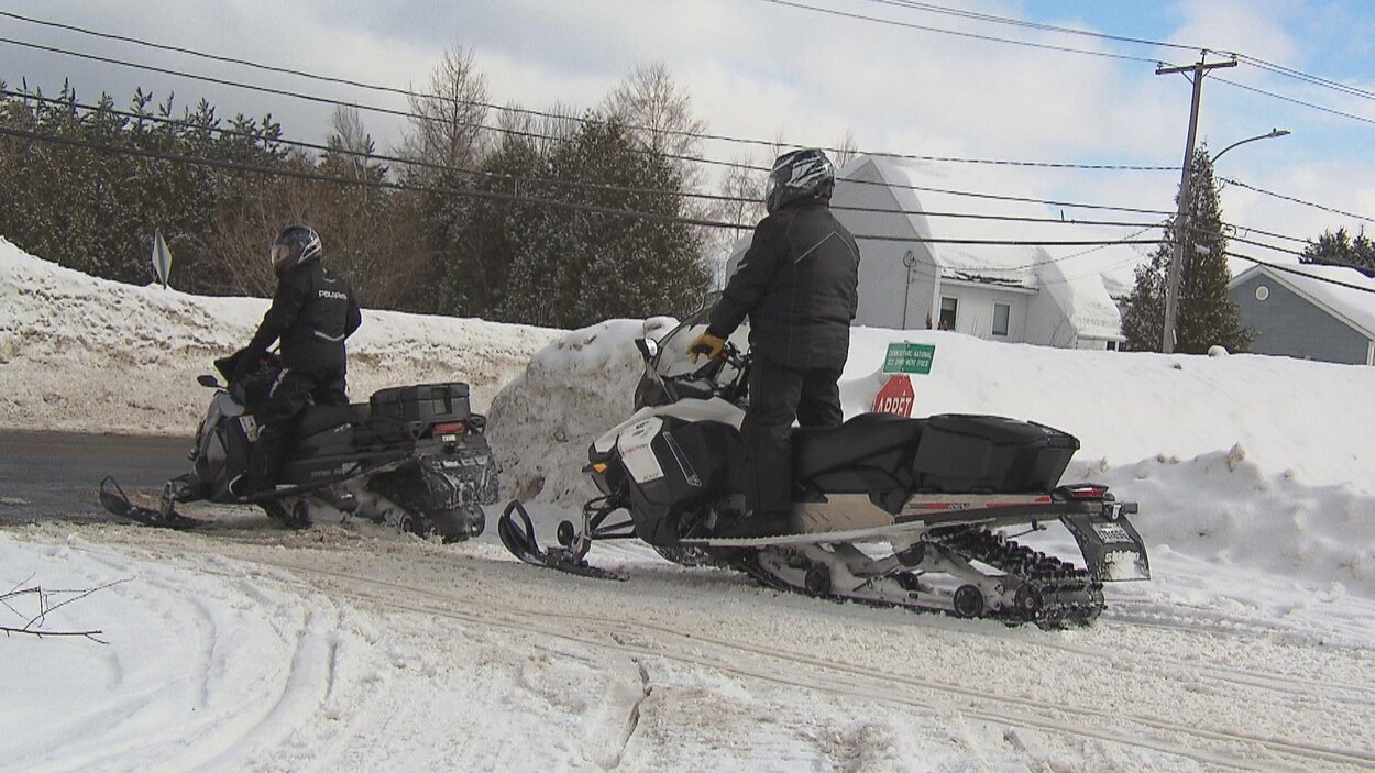 Deux motoneigistes s'apprêtent à traverser une route.