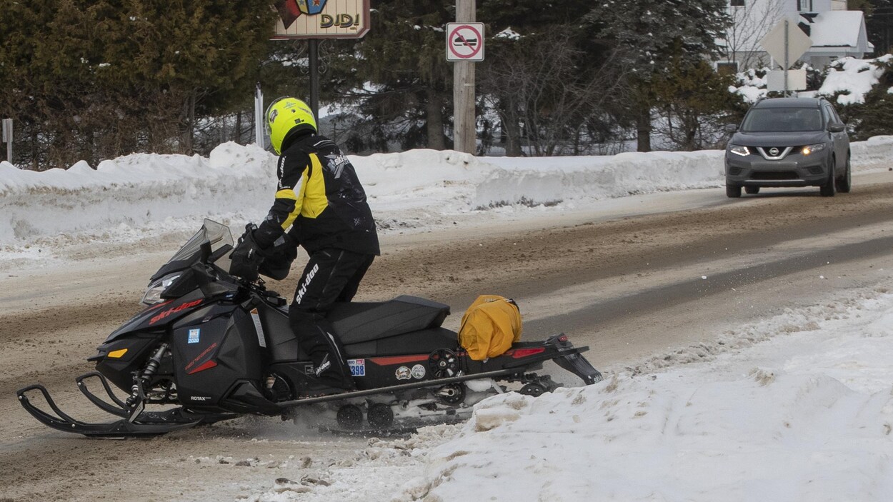 Un motoneigiste s’apprête à traverser une route où l’on voit une voiture au loin.