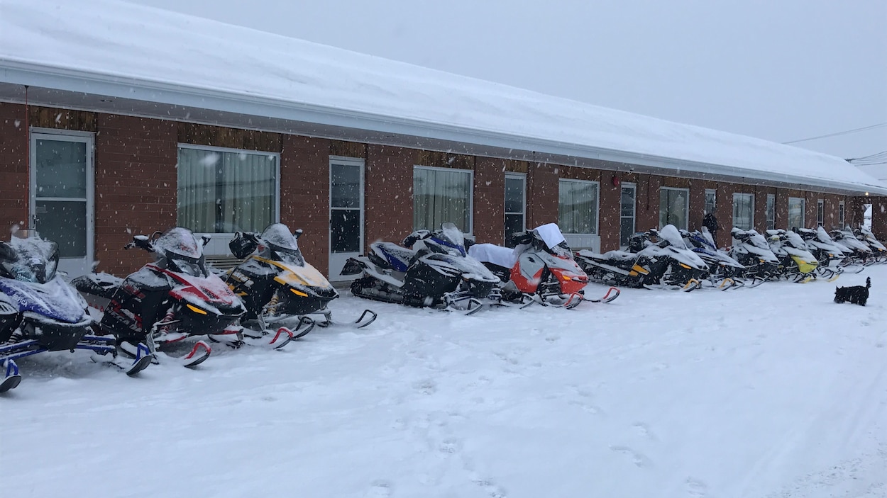 Des motoneiges stationnées devant des chambres d'un hôtel.