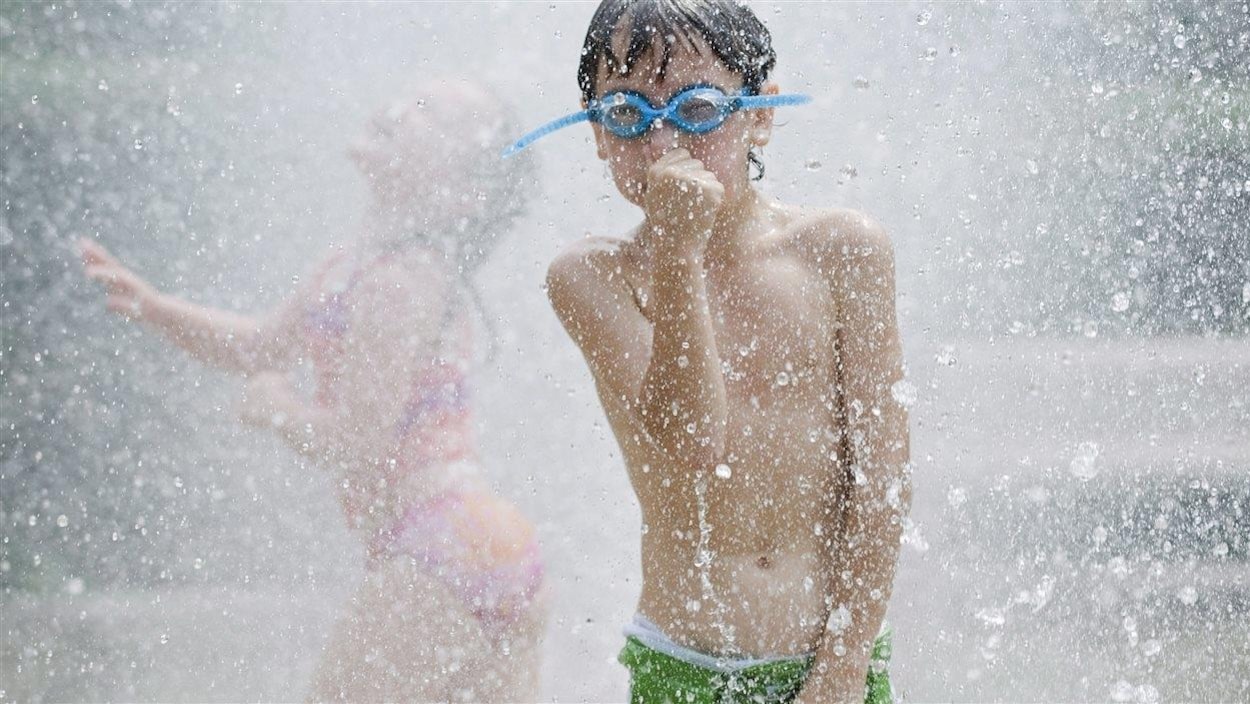 Un garçon portant des lunettes de piscine se fait arroser par un jet d'eau.