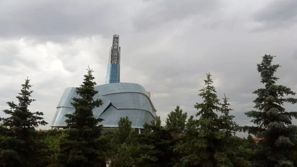 Le Musée canadien pour les droits de la personne vu de l'extérieur derrière des arbres.
