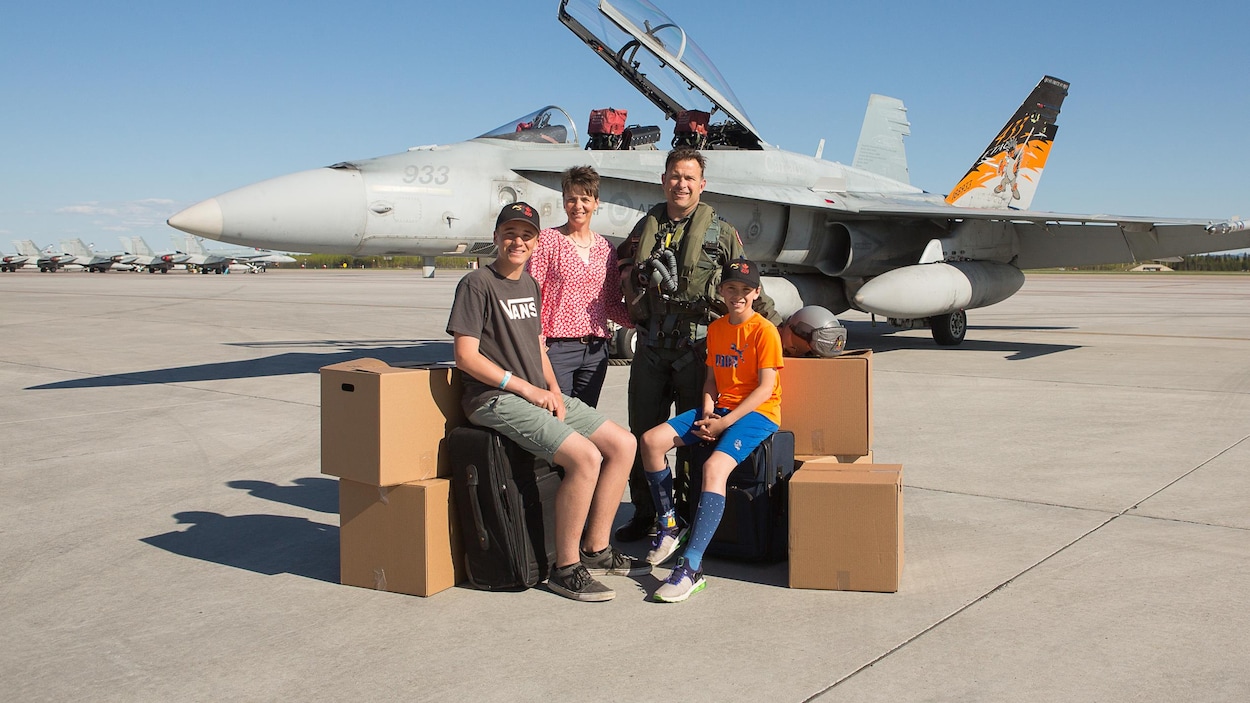 William Radiff, sa conjointe et ses deux fils entourés de boîtes et de valises devant un avion CF-18 stationné sur une piste d'atterrissage.