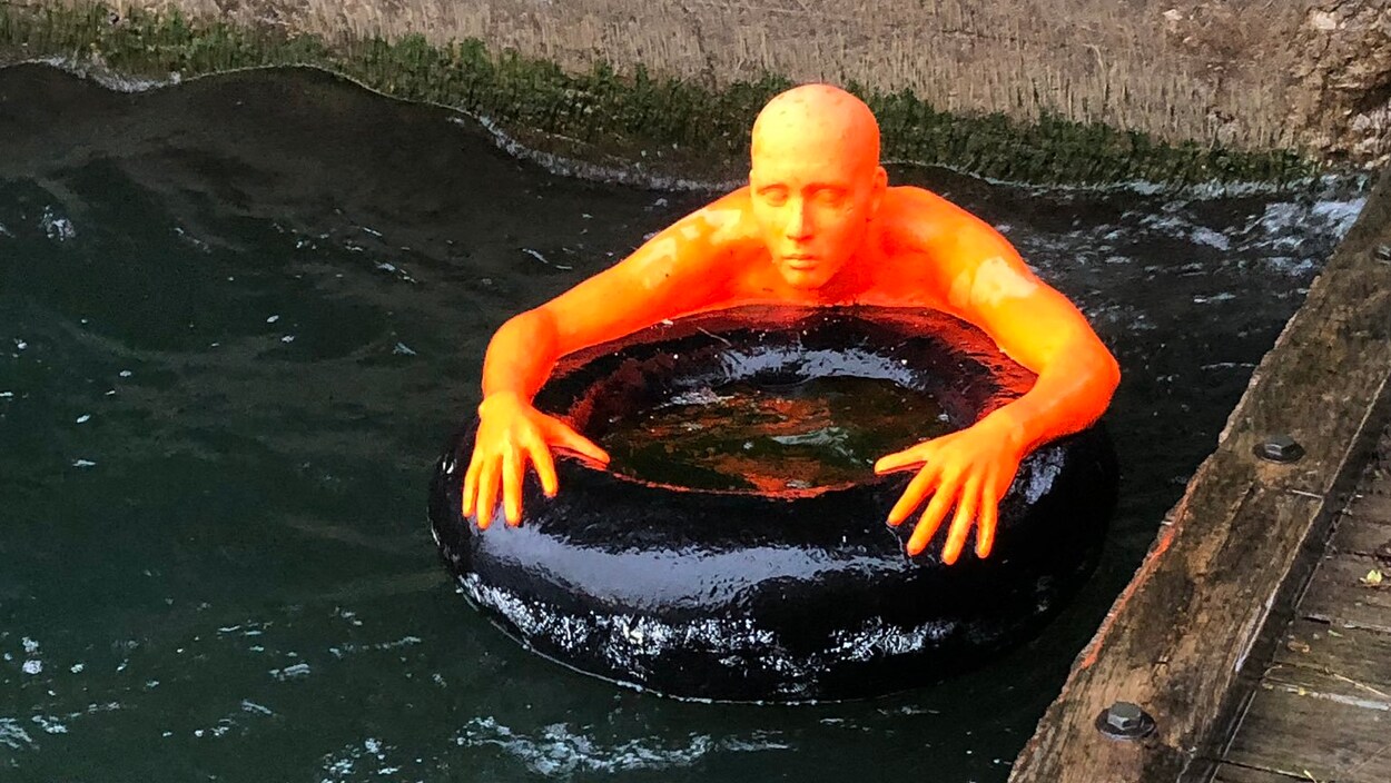 Une effigie représentant un homme orange qui agrippe une bouée noire flotte près d'un quai.