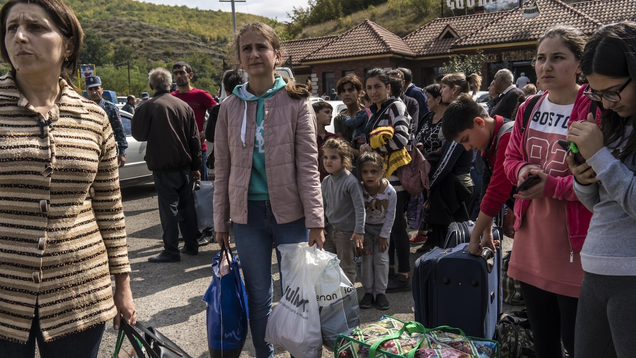 Des femmes et des adolescentes portant des sacs et des valises attendent à l'extérieur.