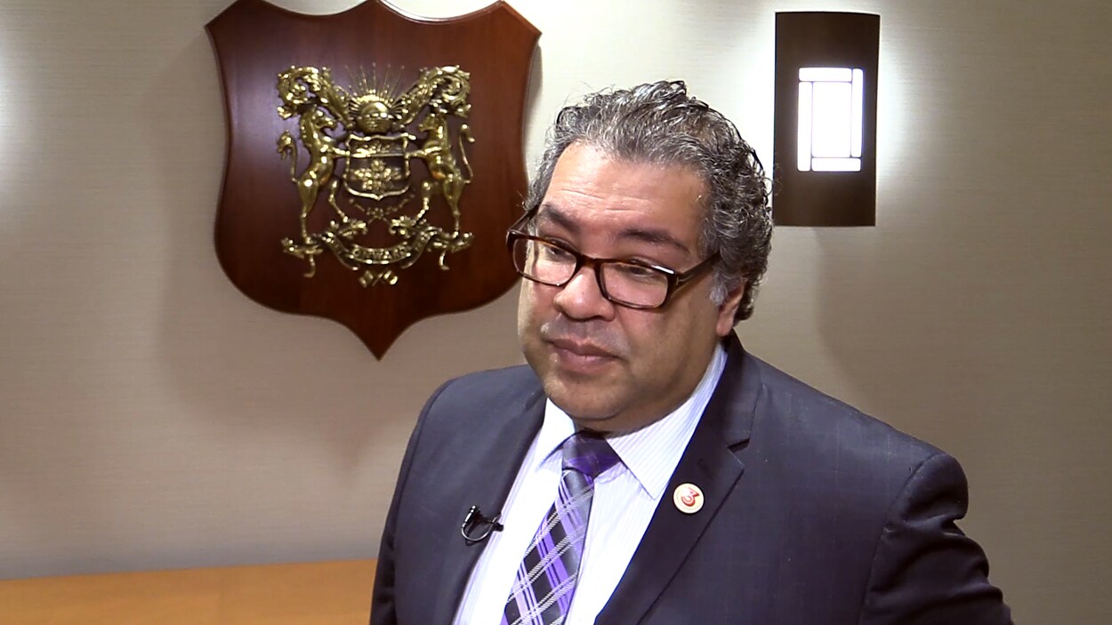 Naheed Nenshi lors d'une entrevue, devant les armoiries de la Ville de Calgary.