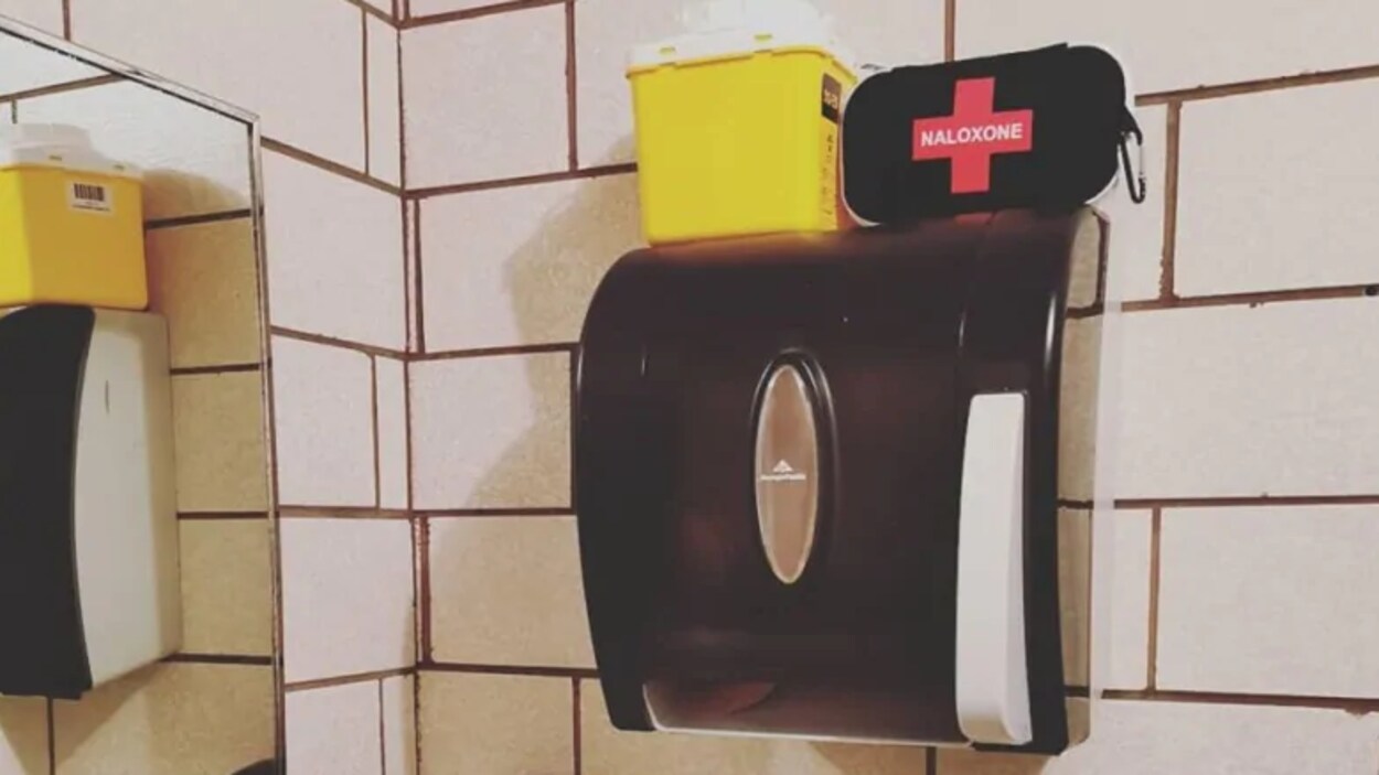 Une trousse de naloxone et un contenant pour seringues souillées au-dessus du distributeur de serviettes de papier.