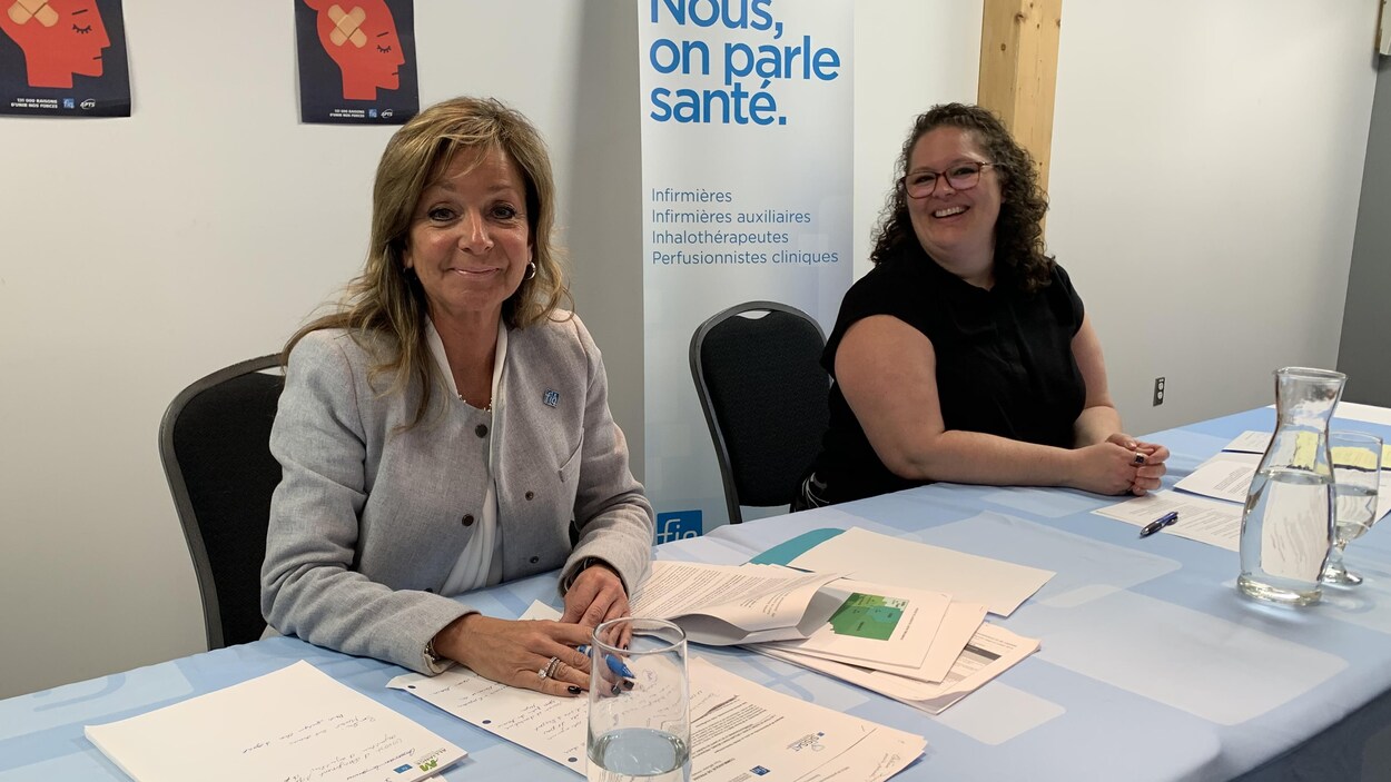 Deux femmes sont assises derrière une table lors d'un point de presse, souriantes.