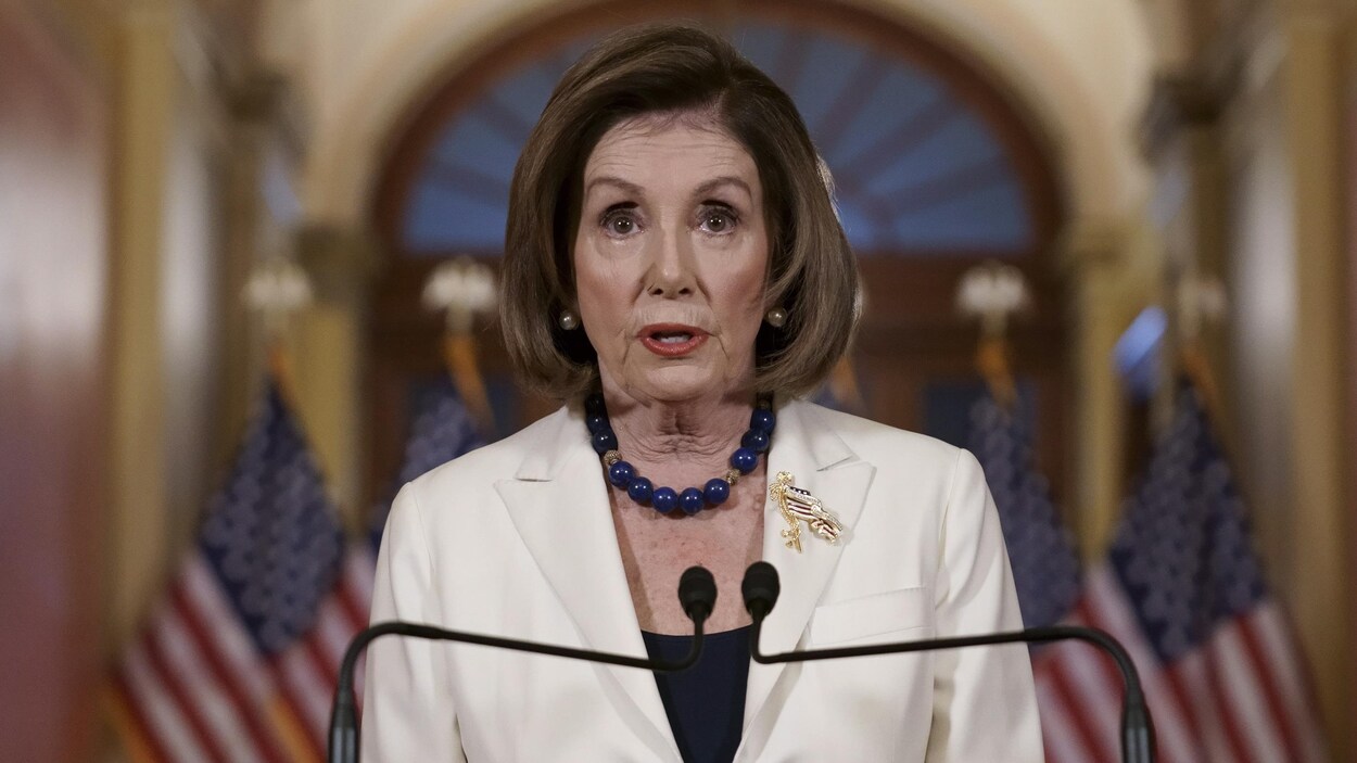 Nancy Pelosi derrière un lutrin avec, derrière elle, des drapeaux des États-Unis.