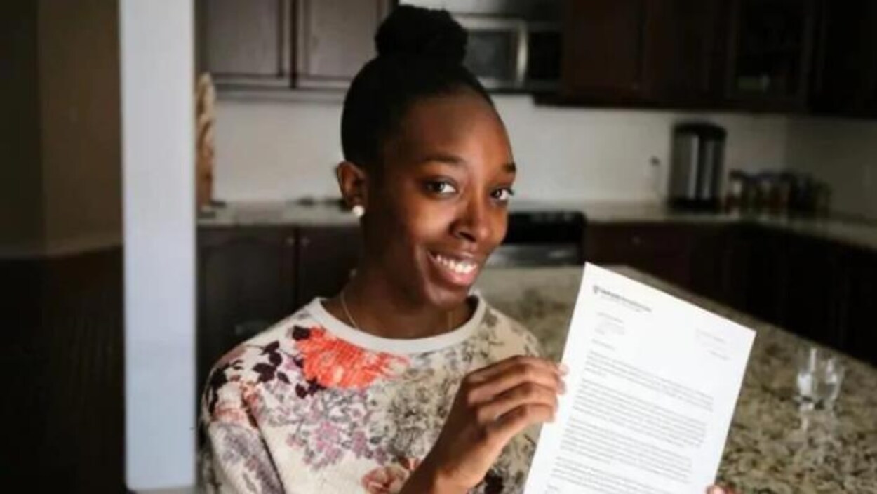 Na'Shantéa Miller avec sa lettre d'admission à Harvard - elle a les cheveux noirs tirés en chignon, elle porte un chandail blanc avec des fleurs, elle a la peau noir, les yeux noirs et elle sourit