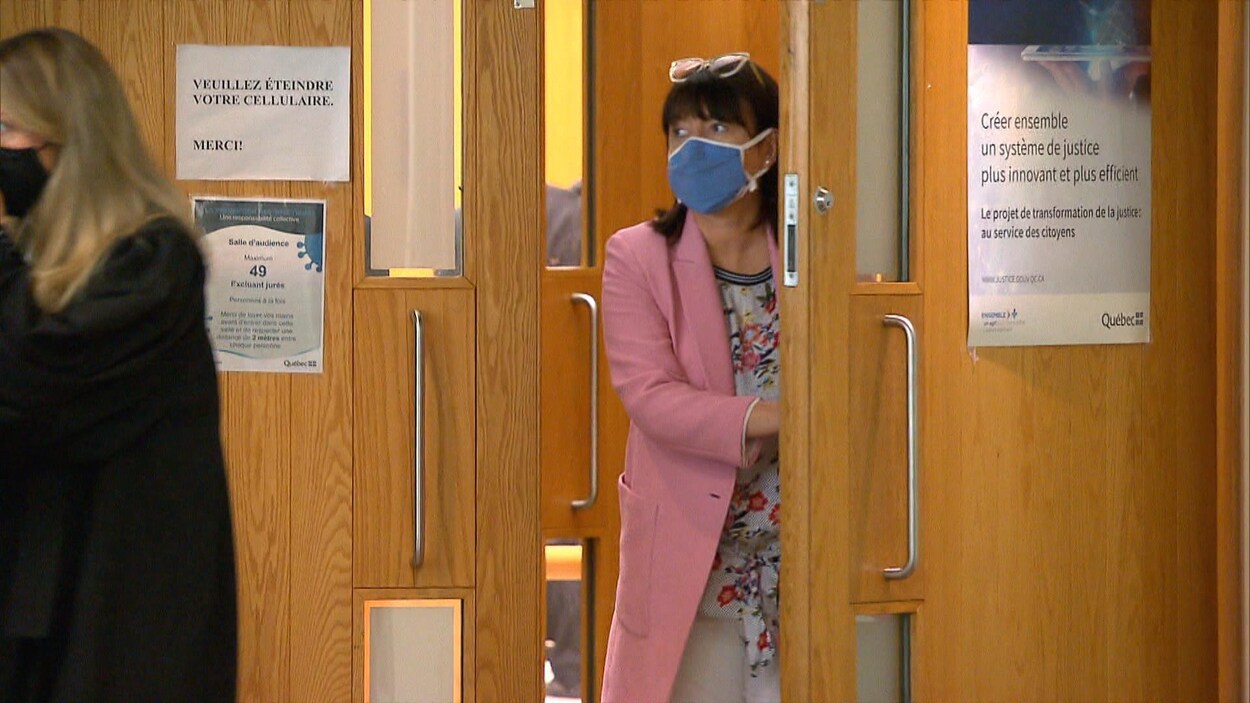 Nathalie Normandeau sort d'une salle d'audience, elle porte un veston rose et un masque.