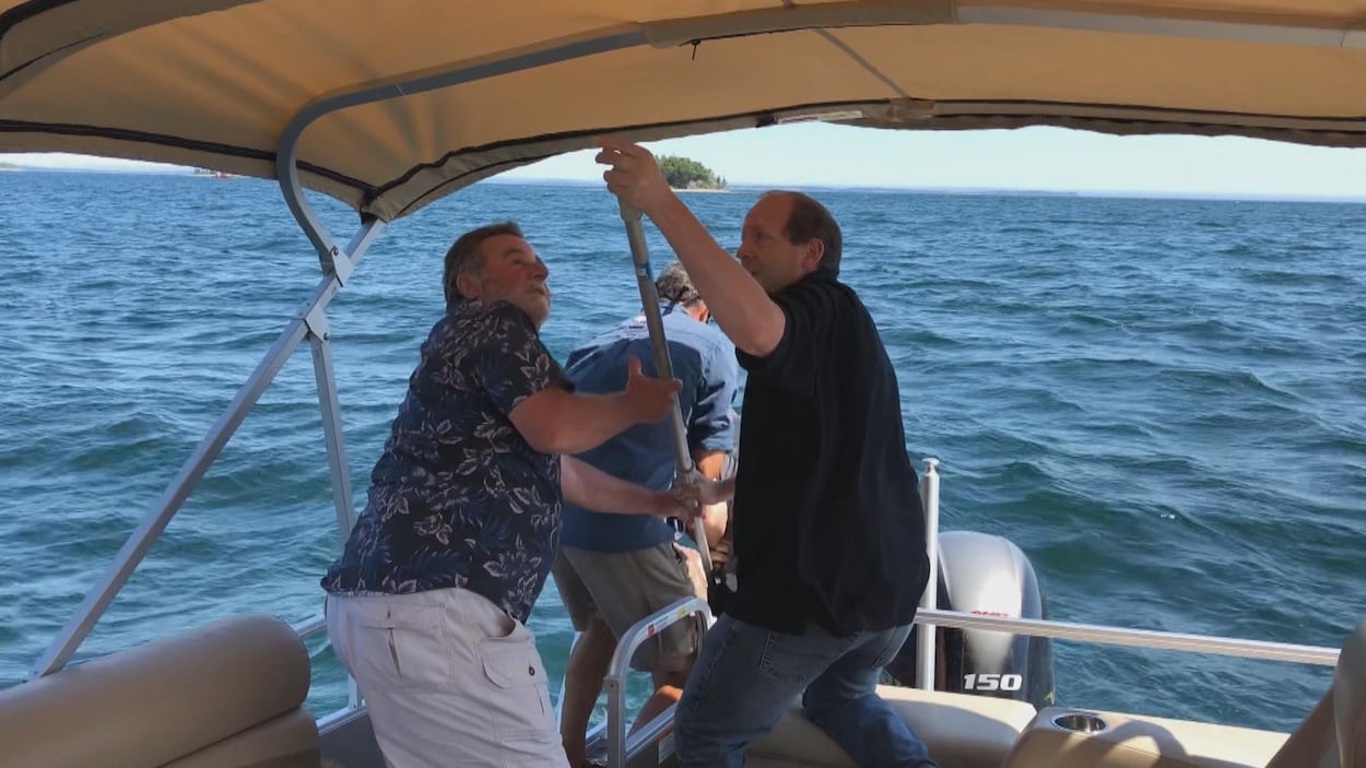 Trois hommes à l'arrière du bateau aident le naufragé à monter à bord.