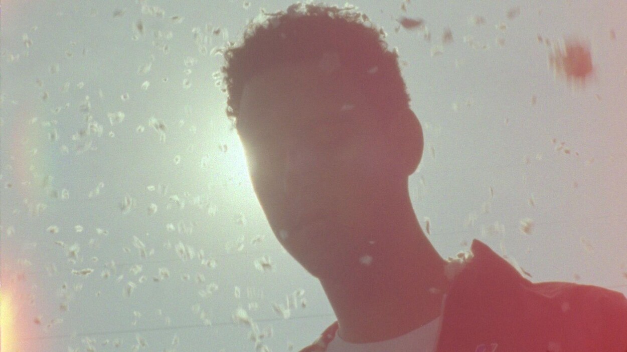 Un jeune homme, en contre-plongée, a la tête juste devant le soleil.