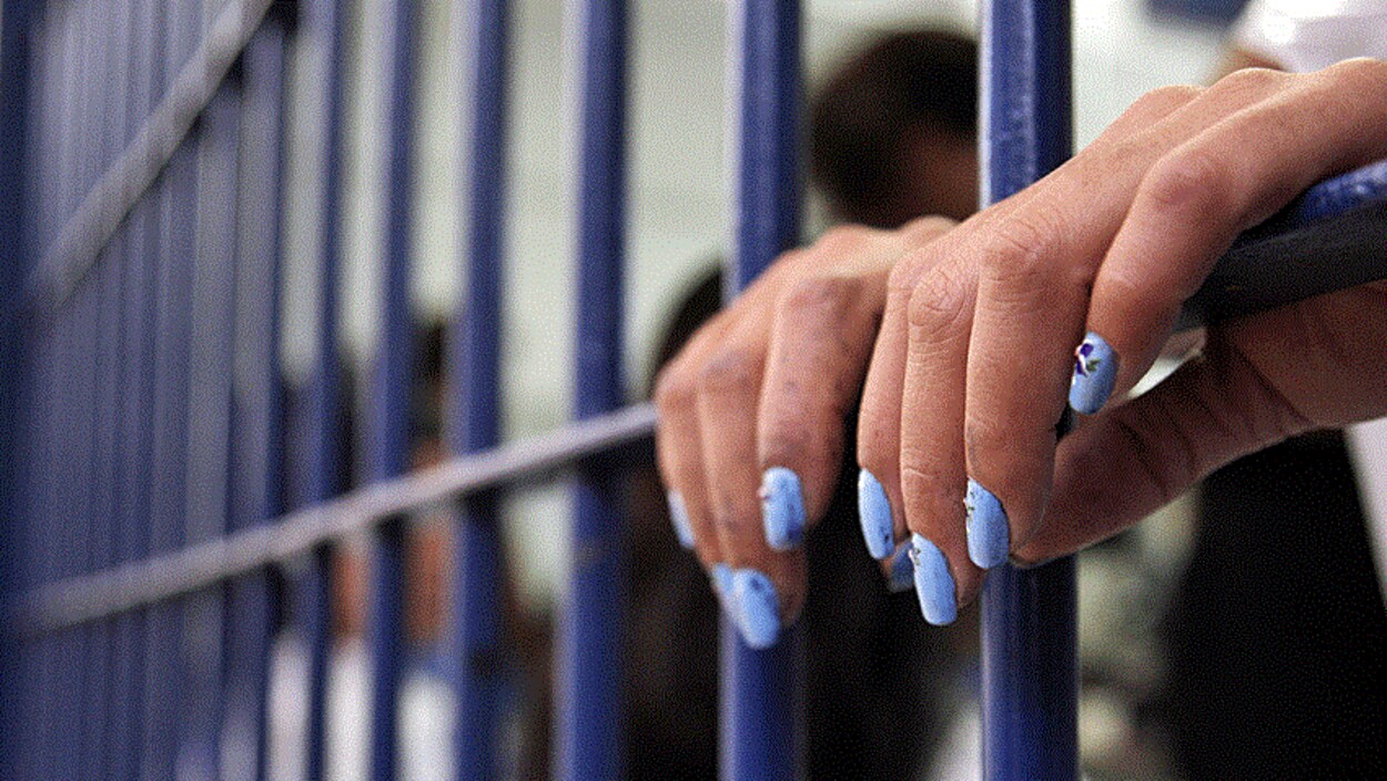 Deux mains de femmes dépassent des barreaux d'une cellule de prison.