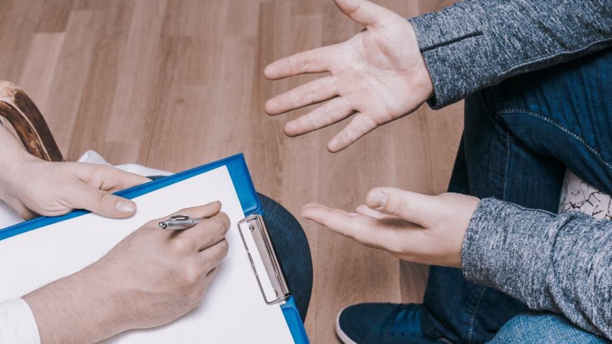 Un médecin prend des notes en présence d'un patient, assis en face de lui.