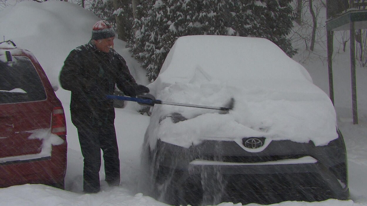 Un homme déneige sa voiture.