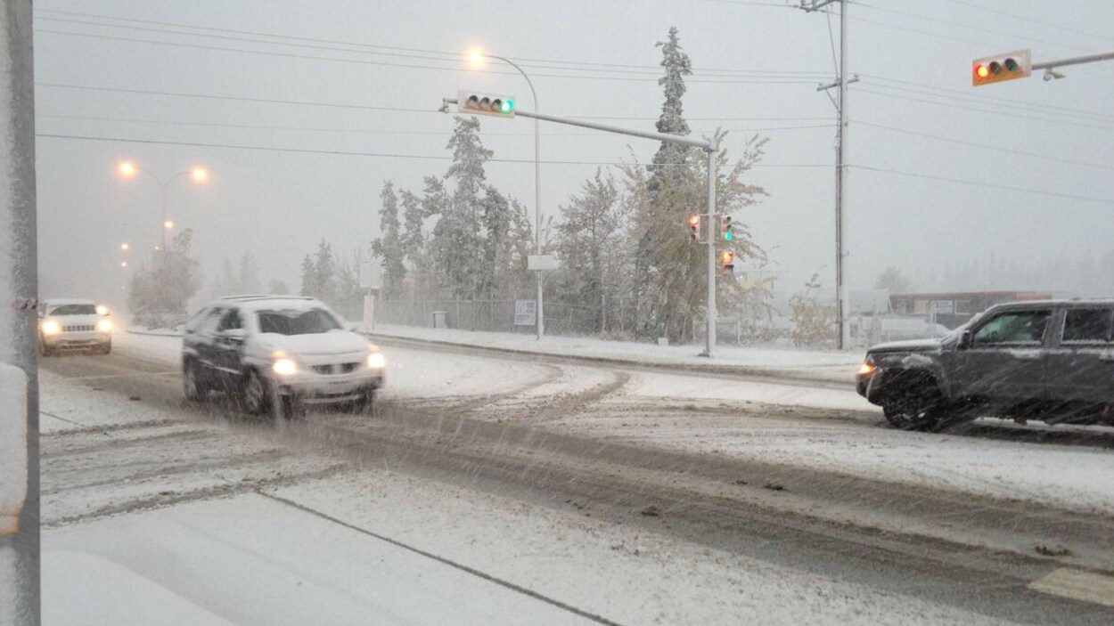 Des voitures avancent doucement sur une route enneigée de Whitehorse.