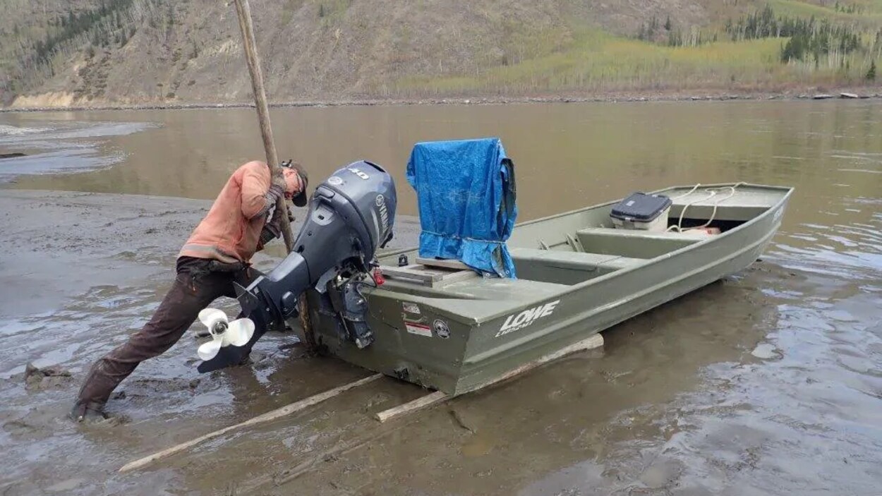Neil Fletcher marche dans la boue en poussant son bateau à moteur dans l'eau.