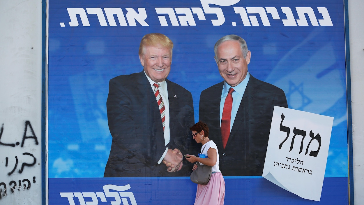 Une femme passant devant une affiche géante montrant Nétanyahou aux côtés de Trump, tout sourire.