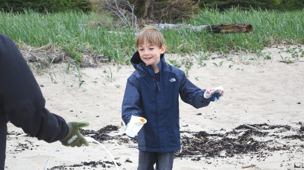 Un jeune homme ramasse une canette et un verre de plastique pour nettoyer la plage à Port-Cartier. Un jeune homme ramasse une canette et un verre de plastique pour nettoyer la plage à Port-Cartier.