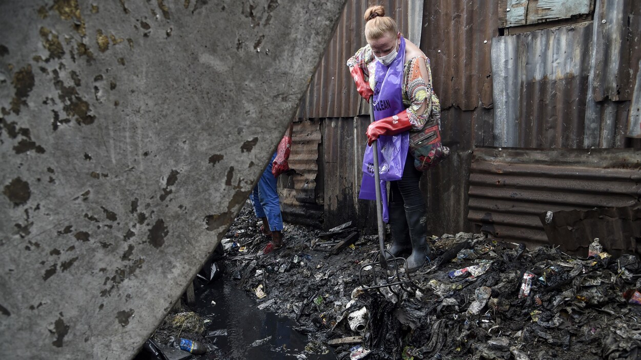 Une femme ramasse des déchets dans un bidonville de Lagos avec une fourche.