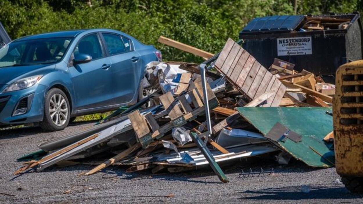 Un tas de débris jonchent le sol devant un conteneur à déchets plein.