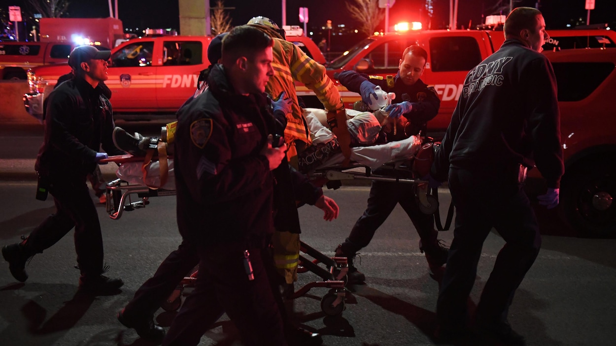 Une personne est couchée sur une civière et des ambulanciers s'affairent autour d'elle en pleine rue à New York. Une personne est couchée sur une civière et des ambulanciers s'affairent autour d'elle en pleine rue à New York.