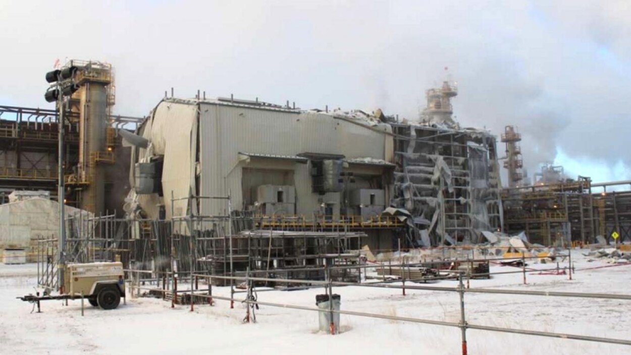 Le mur extérieur d'une usine est endommagé, des panneaux pendent de la charpente et d'autres gisent sur le sol enneigé.