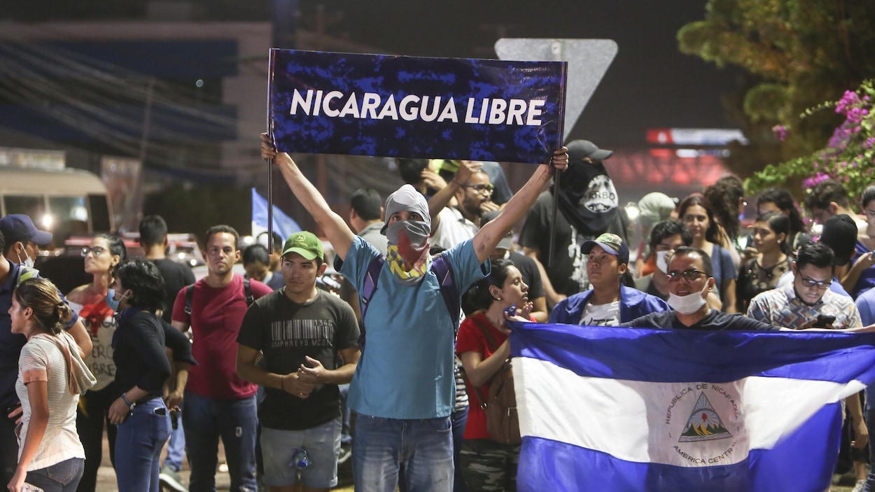 Un homme se tient devant des manifestants avec une affiche où on peut lire «Nicaragua Libre» Un homme se tient devant des manifestants avec une affiche où on peut lire «Nicaragua Libre»