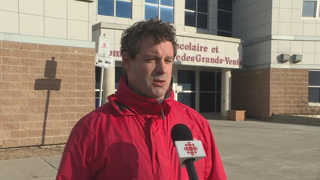 Nick Whalen en entrevue. En arrière-plan se trouve le centre scolaire et communautaire des Grands-Vents à Saint-Jean.